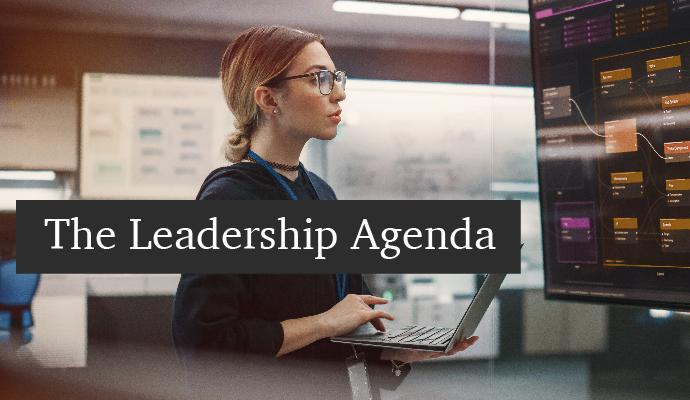 A photograph of a woman with a laptop with whiteboards in the background with the words "The Leadership Agenda" superimposed