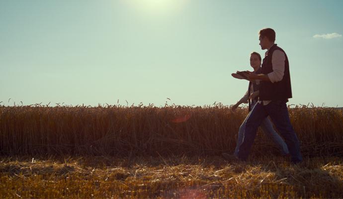 Photo of two people walking with a field of crops in the background