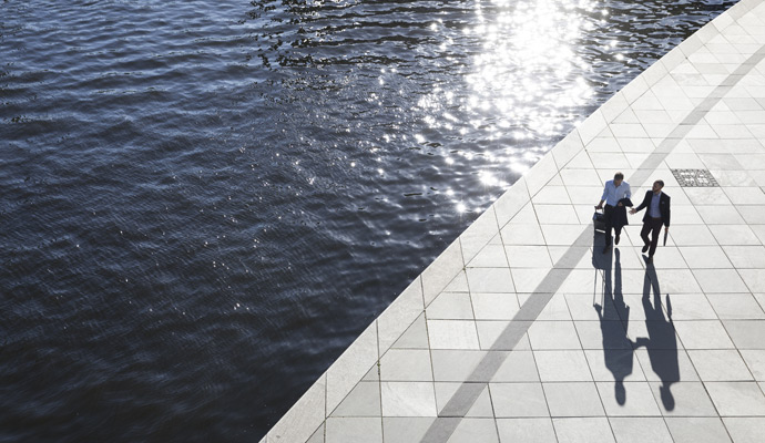 Two business professionals walk along a sunlit waterfront promenade Two business professionals walk along a sunlit waterfront promenade