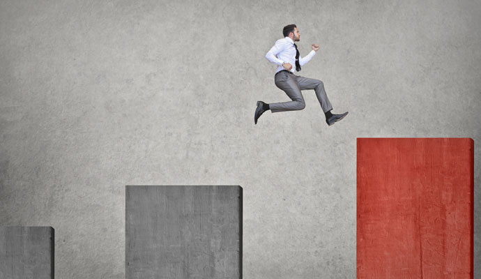 A businessman leaps from a gray bar on a chart to a higher red bar. A businessman leaps from a gray bar on a chart to a higher red bar.