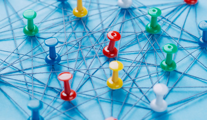 An arrangement of colorful pins linked together with string on a pale blue background suggests a network of connections. An arrangement of colorful pins linked together with string on a pale blue background suggests a network of connections.