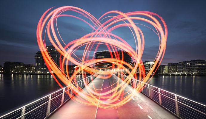 In a time-lapse photo, a glowing, orange light forms circles over a bridge leading to a city