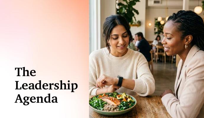 Two people sitting at a table, talking while one checks a smartwatch beside a bowl of food. Two people sitting at a table, talking while one checks a smartwatch beside a bowl of food.