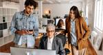 Three casually dressed employees in a modern office meet around a desktop computer.