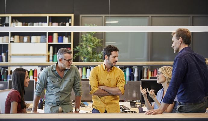 A businesswoman, seated, leads an informal meeting with four casually dressed colleagues.