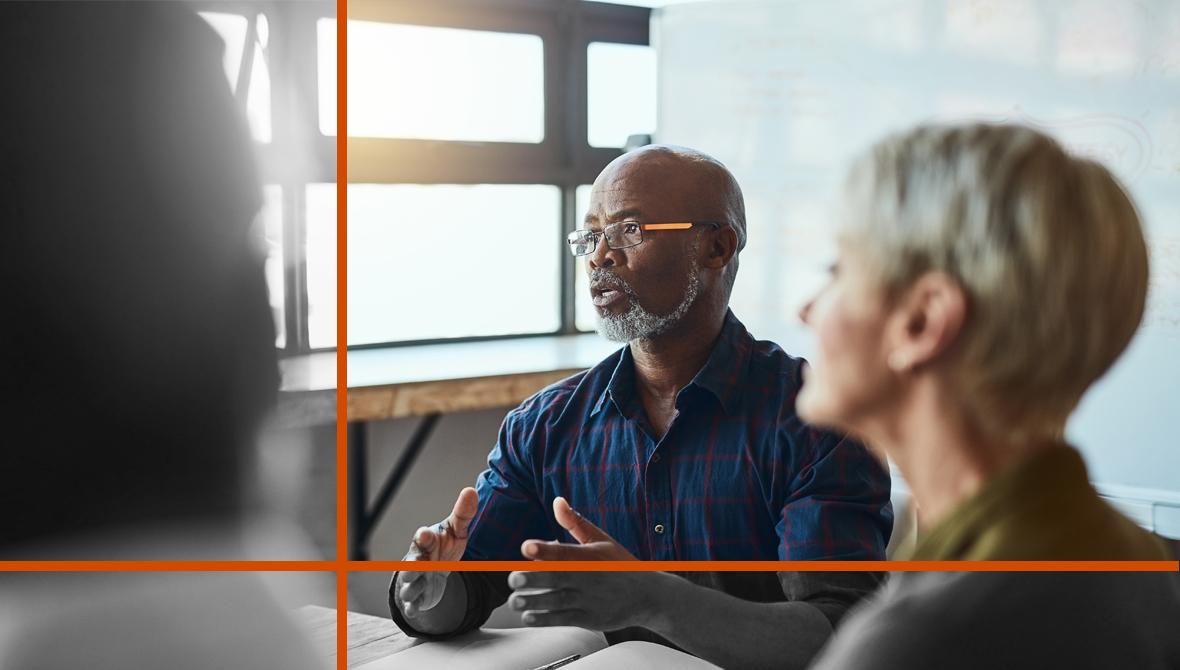 A man sits at the head of a table and leads a discussion with colleagues.