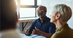 A man sits at the head of a table and leads a discussion with colleagues.