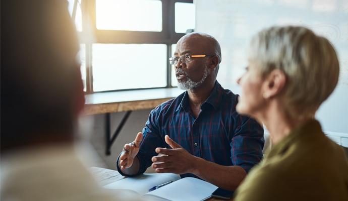 A man sits at the head of a table and leads a discussion with colleagues.