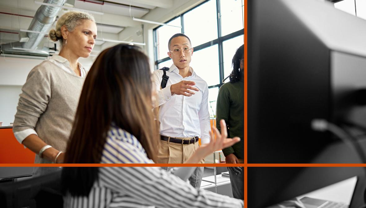 Coworkers meet and gesture toward a computer monitor during a discussion in their office.