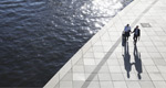 Two business professionals walk along a sunlit waterfront promenade