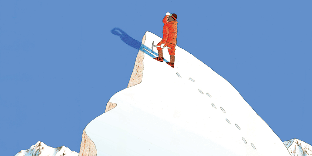 A solo mountaineer, icepick in hand, reaches a high, snowy peak and looks out over the surrounding landscape