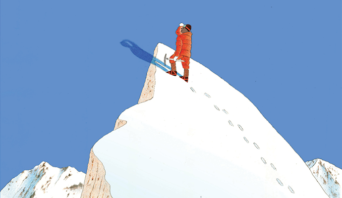 A solo mountaineer, icepick in hand, reaches a high, snowy peak and looks out over the surrounding landscape