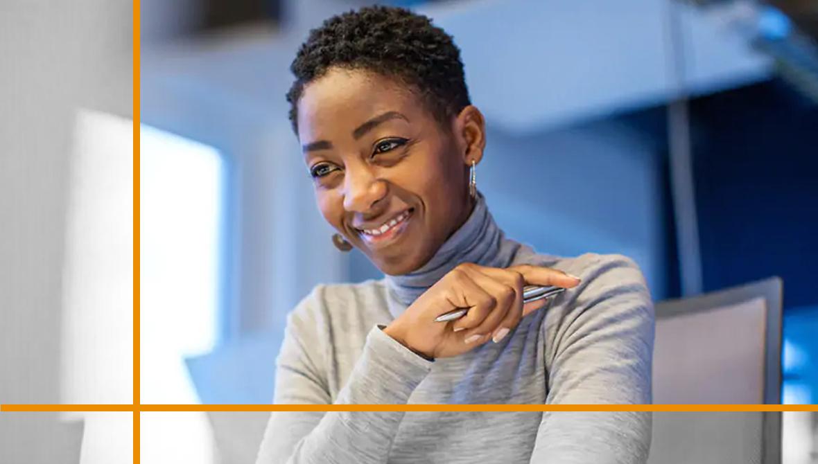 A smiling professional sitting at a desk, holding a pen and looking at a computer screen. A smiling professional sitting at a desk, holding a pen and looking at a computer screen.