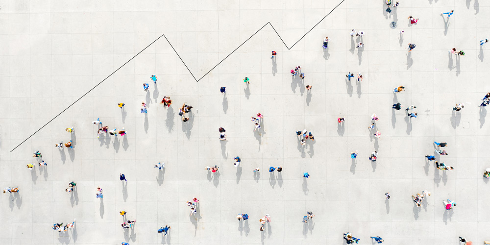 An overhead view of a crowd of people forms the shape of an ascending growth chart. An overhead view of a crowd of people forms the shape of an ascending growth chart.