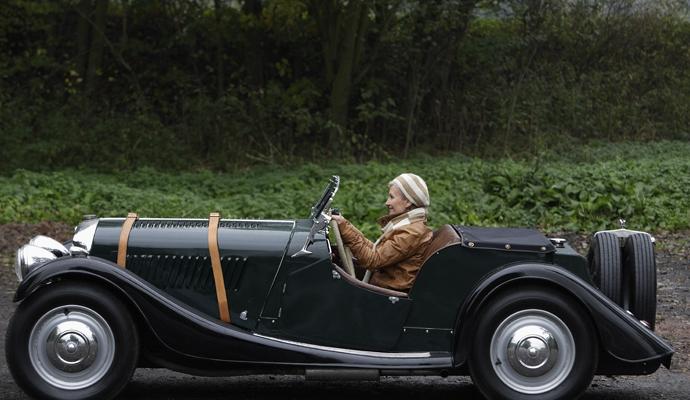A woman drives an early-model classic car on a dirt road A woman drives an early-model classic car on a dirt road