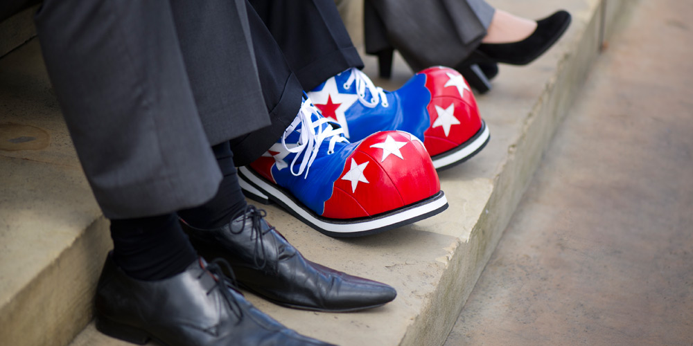 The lower legs of a businessperson in a suit wearing clown shoes