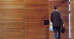 A businessman is seen from behind as he exits the door of a wood-paneled office. 