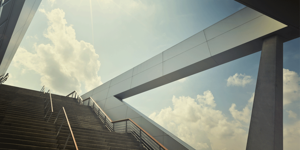 A view up a grand, modern staircase that is open to a blue, sunny sky above. 