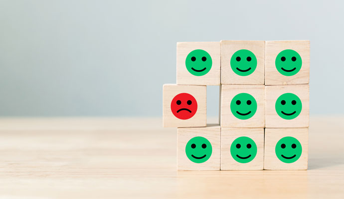 Wooden blocks with cartoon face icons, most of them are smiling, one is frowning  Wooden blocks with cartoon face icons, most of them are smiling, one is frowning
