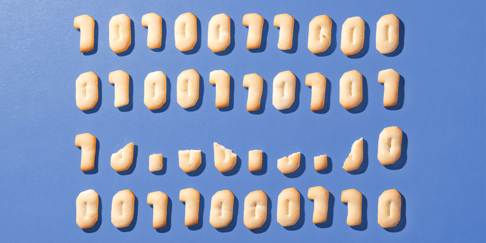 A grid of cookies — including some that are crumbled and broken — baked in the shape of binary code ones and zeros, against a blue background.