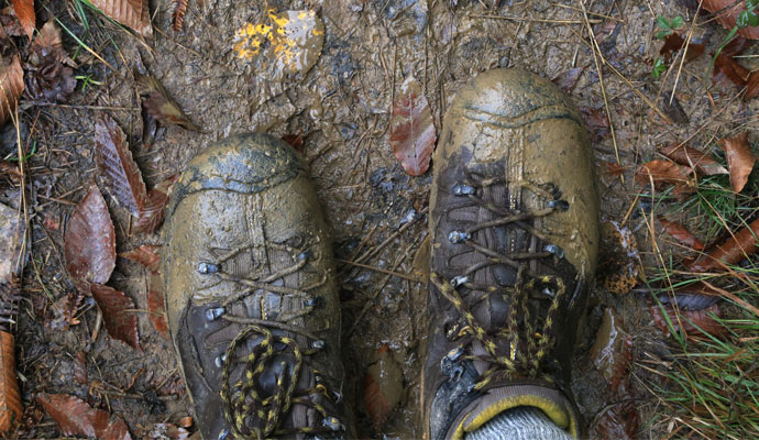An overhead view focuses on a hiker’s pair of mud-covered boots, with leaves, grass, and mud scattered on the trail beneath them. An overhead view focuses on a hiker’s pair of mud-covered boots, with leaves, grass, and mud scattered on the trail beneath them.