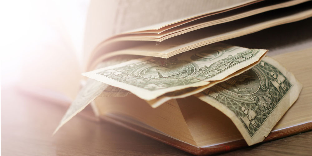 US$1 bills are visible between the pages of an old book. US$1 bills are visible between the pages of an old book.