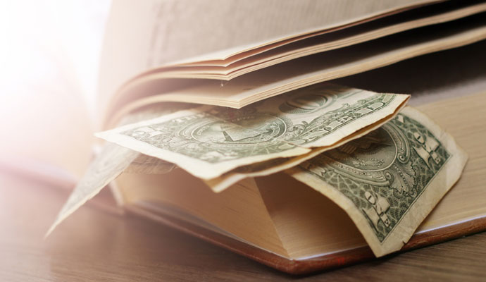 US$1 bills are visible between the pages of an old book. US$1 bills are visible between the pages of an old book.