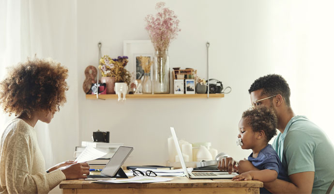 Parents working at a kitchen table while the father holds a baby in his lap Parents working at a kitchen table while the father holds a baby in his lap