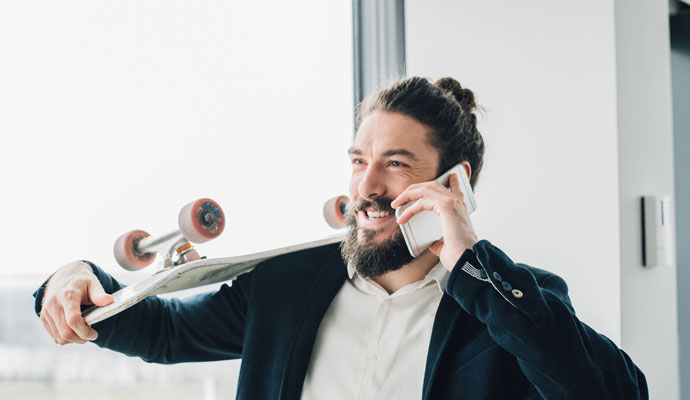 A businessman holds a skateboard over his shoulder while talking on his smartphone. A businessman holds a skateboard over his shoulder while talking on his smartphone.