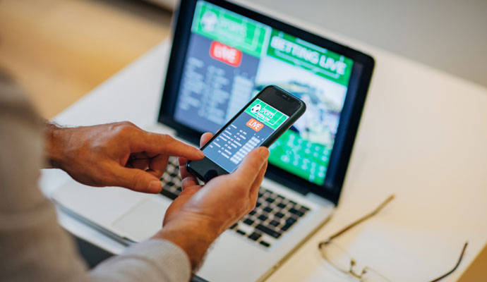 Man places a sports bet on his phone while watching a live game on his laptop Man places a sports bet on his phone while watching a live game on his laptop