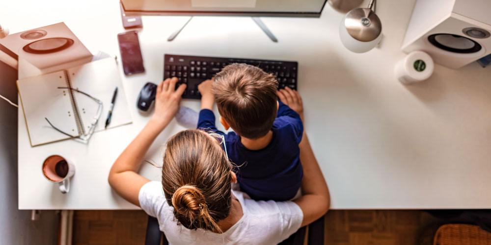 Overhead view of mother working on computer with her young son sitting in her lap. Overhead view of mother working on computer with her young son sitting in her lap.