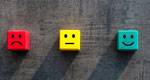 Three colored wooden blocks are next to one another, representing customer satisfaction levels: a red block has a frowning face, a yellow block has a neutral face, and a green block has a smiling face.