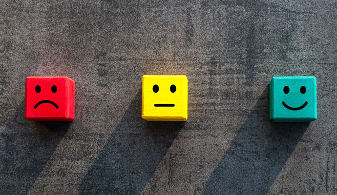 Three colored wooden blocks are next to one another, representing customer satisfaction levels: a red block has a frowning face, a yellow block has a neutral face, and a green block has a smiling face.