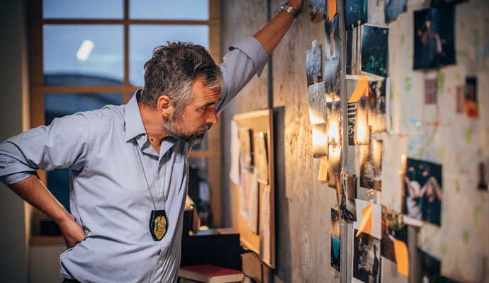 Detective examining clues in a case, arrayed on a bulletin board Detective examining clues in a case, arrayed on a bulletin board