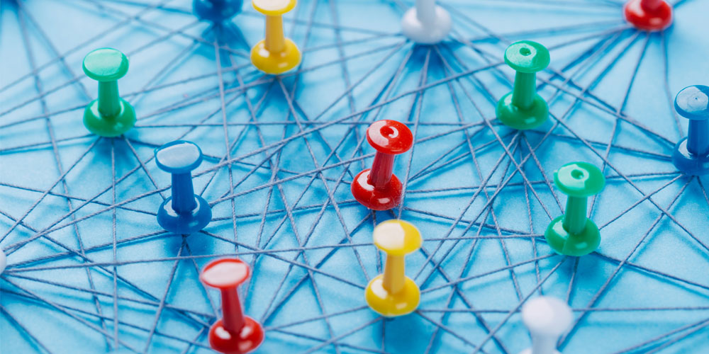 An arrangement of colorful pins linked together with string on a pale blue background suggests a network of connections. An arrangement of colorful pins linked together with string on a pale blue background suggests a network of connections.