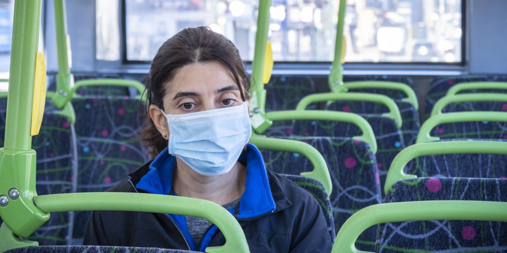 A woman in a surgical mask riding a city bus