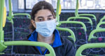 A woman in a surgical mask riding a city bus
