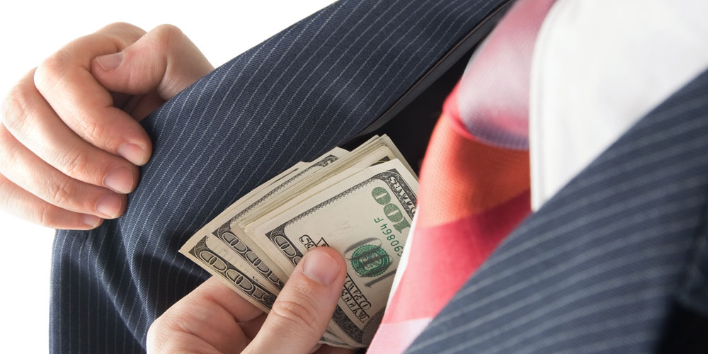 A man dressed in a pinstripe suit furtively pockets $100 bills.