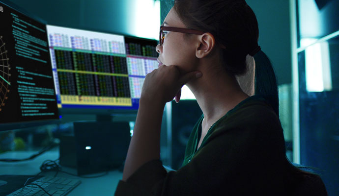 A woman uses multiple computer monitors to analyze data. A woman uses multiple computer monitors to analyze data.