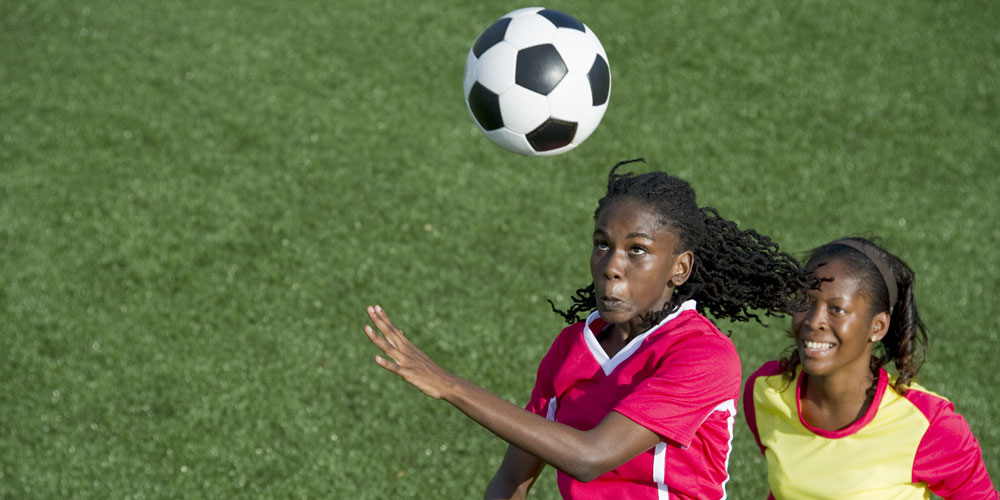 Two women playing soccer vie for an aerial ball.