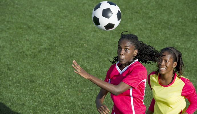 Two women playing soccer vie for an aerial ball. Two women playing soccer vie for an aerial ball.