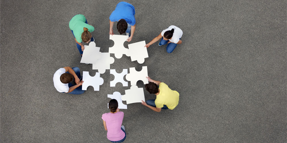 Six people seen from above, putting together giant jigsaw puzzle pieces