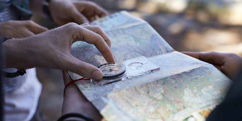 Close-up photo of a map and compass held by many hands Close-up photo of a map and compass held by many hands