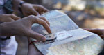 Close-up photo of a map and compass held by many hands