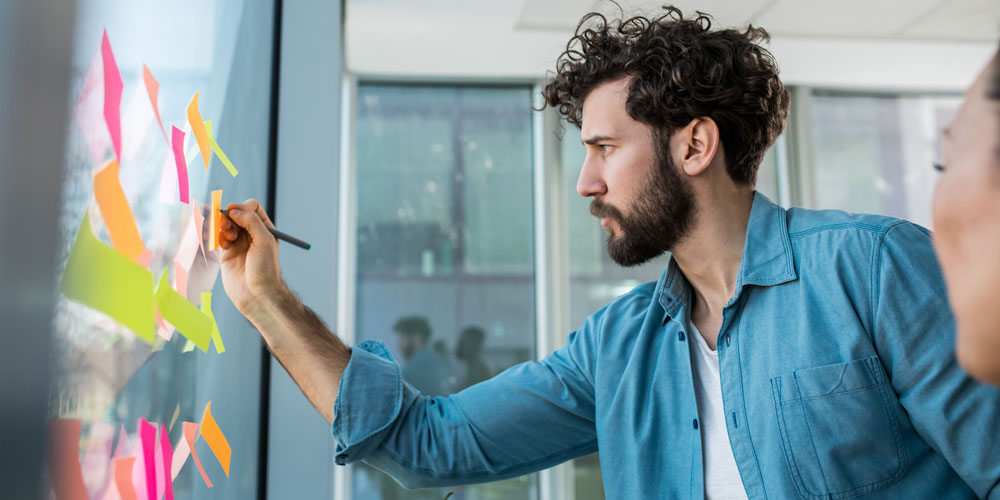 A young worker organizes his ideas by posting sticky notes on a window. A young worker organizes his ideas by posting sticky notes on a window.