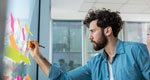 A young worker organizes his ideas by posting sticky notes on a window.