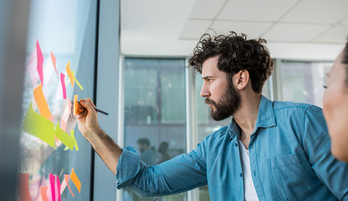 A young worker organizes his ideas by posting sticky notes on a window.