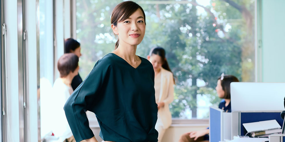 Smiling woman in an office with her team behind her  Smiling woman in an office with her team behind her