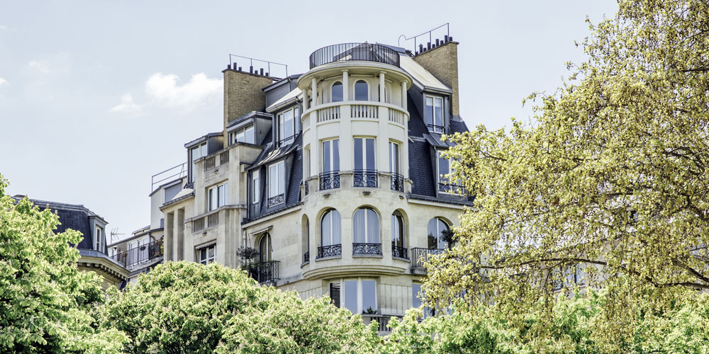 A luxury building looms beyond a row of trees.