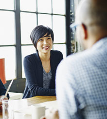 Three coworkers sit at a conference room table, talking and smiling.